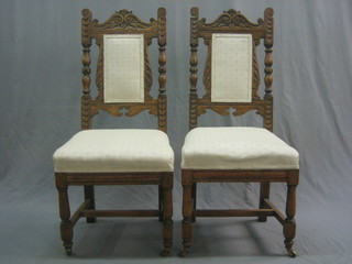 A pair of Edwardian carved oak dining chairs with upholstered seats and backs, raised on turned and block supports