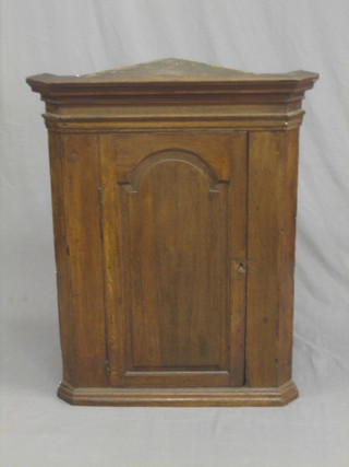 An 18th/19th oak hanging corner cabinet with moulded cornice, the shelved interior enclosed by an arched panelled door 27"