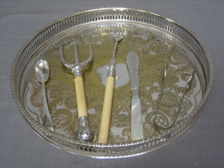 A circular silver plated galleried tea tray, a pair of sugar tongs, 6 pastry forks, a butter knife with mother of pearl handle, a pickle fork, a toast fork and a jam spoon