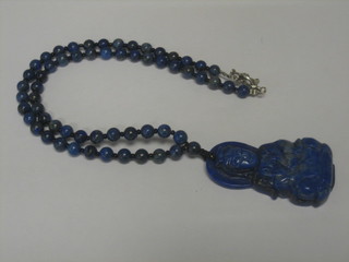 A Lapis Lazuli pendant in the form of a Deity hung on a string of beads