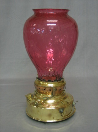 A circular brass twin handled burner/heater with associated red glass shade
