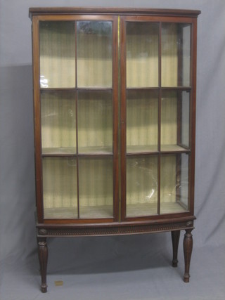 A walnut bow front display cabinet, fitted shelves enclosed by astragal glazed panelled doors, raised on turned and reeded supports 38"