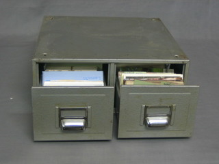A metal 2 drawer table top filing cabinet containing a collection of various postcards