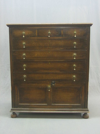 A 1930's Jacobean style oak chest of 3 short and 4 long drawers with cupboard below, raised on bun feet 36"