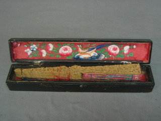 An Eastern carved wooden fan painted court scenes contained in a lacquered box