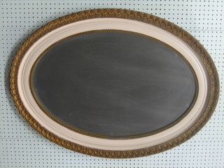 An oval bevelled plate wall mirror contained in a gilt and cream frame 36"