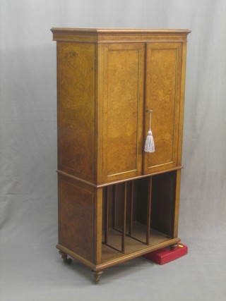 A Victorian figured walnut music cabinet, the interior fitted sliding trays above a recess, raised on turned supports ending in brass caps and castors 24"