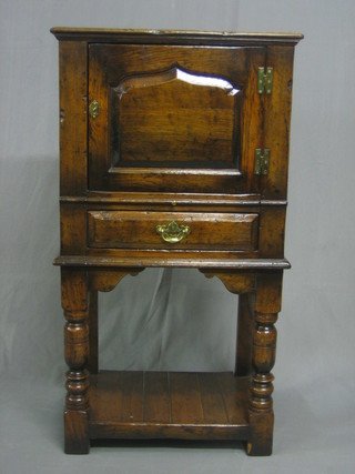 A reproduction 17th Century style carved oak cabinet enclosed by panelled doors, the base fitted a brushing slide above 1 long drawer, raised on turned and block supports with undertier 25"