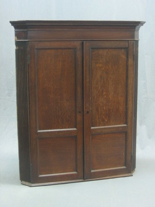 A Georgian oak hanging corner cabinet with moulded cornice, the interior fitted 2 shaped shelves and having 3 spice drawers to the base, enclosed by panelled doors and with reeded decoration to the sides 36"