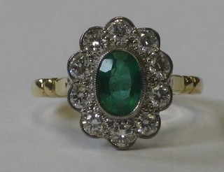 An 18ct yellow gold dress ring set an oval cut emerald surrounded by numerous diamonds approx 0.60/0.75ct