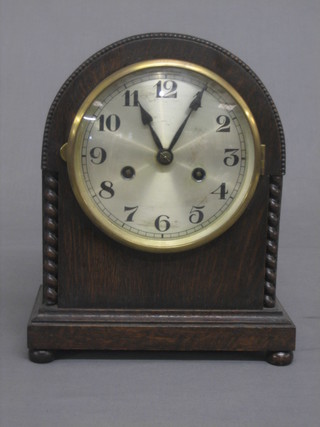 An 8 day striking mantel clock with silvered dial and Arabic numerals contained in an oak arch shaped case