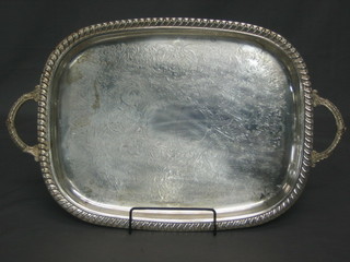 An oval silver plated twin handled tea tray with engraved decoration and gadrooned borders, raised on 4 panelled feet 22"