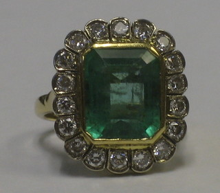 An 18ct yellow gold dress ring set a rectangular cut emerald supported by numerous diamonds