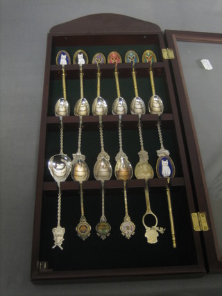 A mahogany display cabinet containing a collection of various collectors spoons