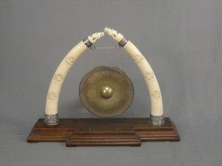 An Eastern dinner gong supported by 2 carved Eastern ivory tusks, raised on a stand 33"