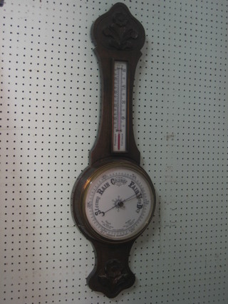 An Edwardian aneroid barometer and thermometer contained in a carved oak wheel case