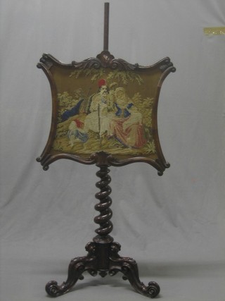 A Victorian mahogany pole screen with shaped Berlin woolwork banner raised on a spiral turned column tripod base