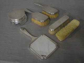 A silver backed 6 piece dressing table set comprising hand mirror, pair of hair brushes, pair of clothes brushes, circular jar and cover with engine turned silver lid, London 1951, 53 and 54