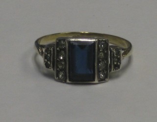 A gold dress ring set a rectangular cut blue stone supported by "diamonds"