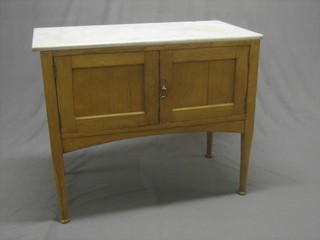 An Art Nouveau honey oak wash stand with white veined marble top, the base fitted a cupboard enclosed by panelled doors and raised on turned supports 36"