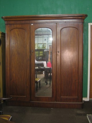 A Victorian mahogany triple wardrobe with moulded cornice enclosed by an arched panelled door flanked by a pair of panelled doors, raised on a platform base 79"