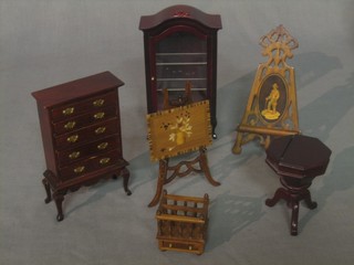 A collection of mahogany dolls house furniture including 2 easels, a 2 division Canterbury, a conical shaped work box, a tall boy and a display cabinet