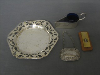 A circular silver plated dish with pierced rim, a wedge shaped silver plated salt, a decanter label and a gold plated cigar cutter