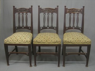 A set of 3 Edwardian Art Nouveau carved mahogany stick and bar back dining chairs with upholstered seats, raised on square tapering supports