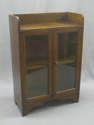 A 1930's oak bookcase with three-quarter gallery, fitted adjustable shelves enclosed by glazed panelled doors, raised on bracket feet 24"