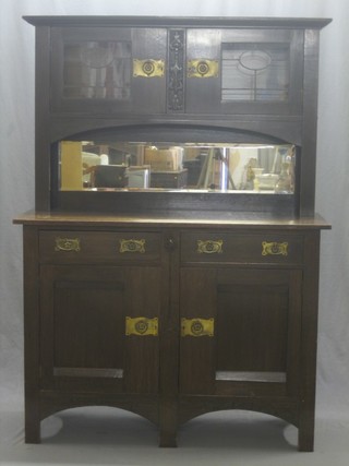 An oak Art Nouveau dresser, the raised back fitted cupboards enclosed by lead glazed panelled doors, the recess with mirrored panel above 2 short drawers, the base fitted 2 cupboards enclosed by panelled doors 49"
