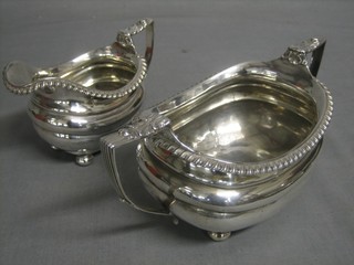 A George III silver twin handled sugar bowl with gadrooned decoration together with a matching cream jug, raised on bun feet, London 1818, 17 ozs