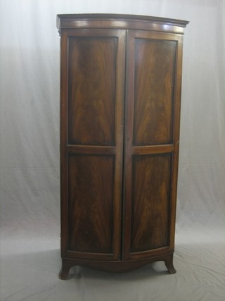 A Georgian style mahogany bow front wardrobe with moulded cornice enclosed by panelled doors and raised on splayed bracket feet 32"