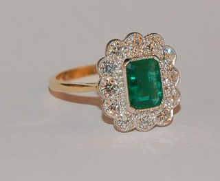 A lady's 18ct yellow gold dress ring set a lozenge cut emerald supported by numerous diamonds, approx 1.05/1.35ct