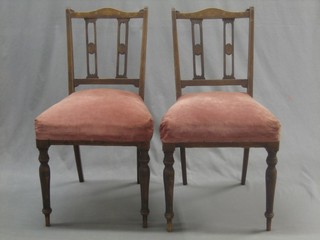 A pair of Edwardian inlaid mahogany bedroom chairs the seats upholstered in pink material and raised on turned supports