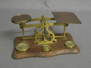 A pair of brass letter scales raised on an oak base with weights 9"