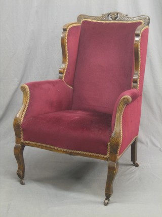An Edwardian show frame mahogany winged armchair upholstered in red material and raised on cabriole supports
