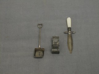 A silver napkin grip, a silver salt spoon in the form of a shovel and a silver bladed book mark in the form of a knife