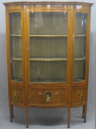 A handsome Edwardian Sheraton style satinwood display cabinet of serpentine outline and with moulded cornice, painted swags, the interior fitted shelves enclosed by glazed panelled doors, raised on square tapering supports ending in spade feet 50"
