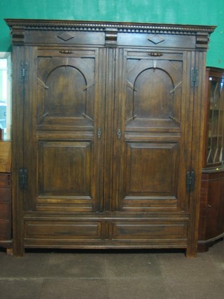 A large and impressive 1930's carved oak armoire with moulded and dentil cornice enclosed by panelled arch shaped doors and of panelled construction 73"