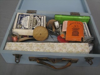 A blue painted wooden box with hinged lid containing a collection of various knitting needles, crochet hooks etc