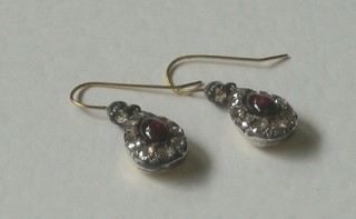 A pair of cabouchon cut garnet drop earrings surrounded by diamonds
