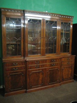 A handsome Georgian style mahogany triple breakfront bookcase with moulded cornice, the interior fitted adjustable shelves enclosed by astragal glazed panelled doors, the base fitted 2 long drawers above a double cupboard flanked by 2 drawers above cupboards enclosed by panelled doors, raised on a platform base 90"
