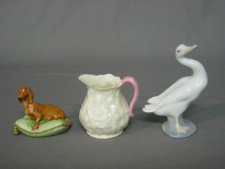 A Lladro figure of a goose 5", a Beleek white glazed jug 3" (chip to rim) and a porcelain figure of a seated brown Dachshund 3"