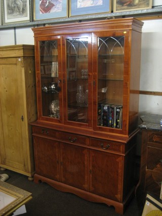 A Georgian style yew bookcase on cabinet, the upper section with moulded and dentil cornice, fitted adjustable shelves enclosed by glazed panelled doors, the base fitted 3 long drawers above a triple cupboard, raised on bracket feet 50" 