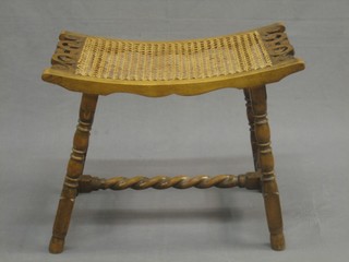 A beech saddle shaped stool with woven cane seat, raised on bobbin turned supports and spiral turned H framed stretcher, 21"