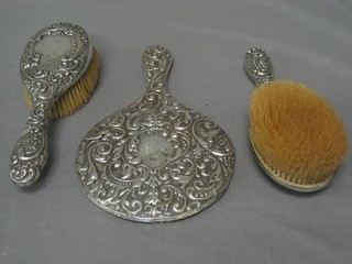 A 3 piece embossed silver backed dressing table set with pair of hair brushes and a hand mirror