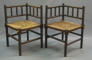 A pair of oak corner chairs with bobbin turned decoration and woven rush seats, raised on turned supports