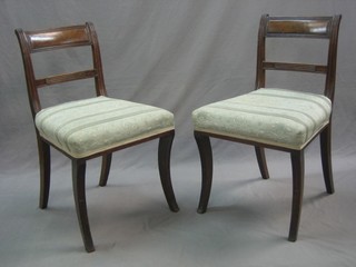 A pair of Regency mahogany bar back dining chairs with plain mid rails and upholstered seats, raised on sabre supports