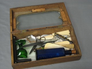 A rectangular wooden box with glazed hinged lid containing a 3 pronged fork, 4 pocket knives and other curios