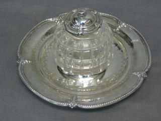 A Victorian circular cut glass inkwell with hinged silver lid, raised on a circular silver tray London 1877, 5 ozs